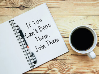 Open notebook with text “If you can’t beat them, join them” and a cup  of coffee on wooden background.