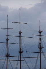 three wooden masts of a Dutch fluyt merchant sailing ship of XVIII century on a grey sky and clouds background close up vertical view