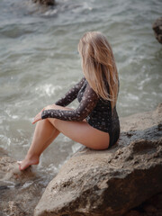 Portrait of attractive blonde woman with long hair posing on rocky beach.