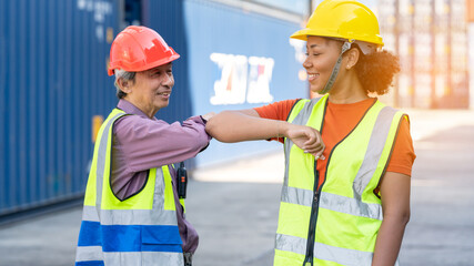  Warehouse business. A Chinese man and a african american woman in safety suit elbow bump and conclude a job for transport and logistics after  Successfully completed business Contract