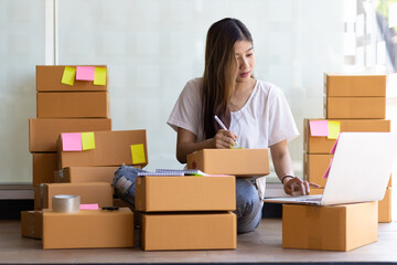 A young woman running a small online business is writing a shipping address on a parcel.