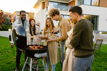 White man grilling meat during barbeque with his friends on backyard - obrazy, fototapety, plakaty