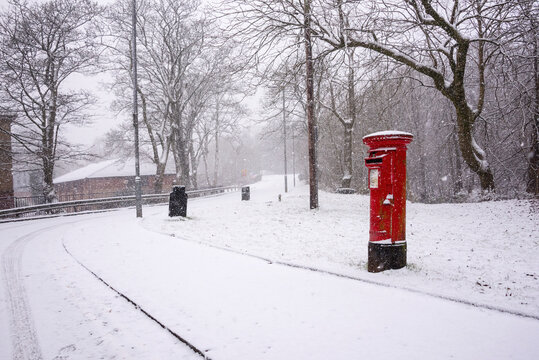 Red post box in snow in rural Scottish setting.