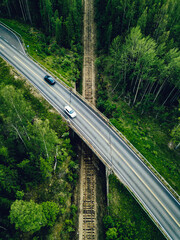 Aerial view of country road above the railway in a green summer forest