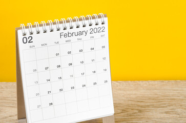 February 2022 desk calendar on wooden table with yellow background.