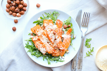 Healthy vegan balanced Salad of baked pumpkin, arugula, parmesan and hazelnuts. View from above.