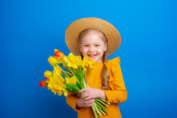 cute little girl in a straw hat holding a bouquet of spring flowers on a blue background,