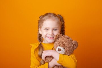 cute little girl holding a teddy bear on a yellow background, hugging