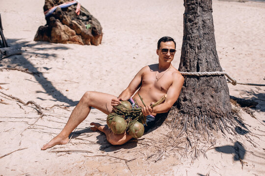 Cinfident adult male model in sunglasses and beach clothes holding on to coconuts and looking into the distance. Summertime concept.