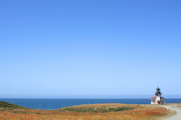 Distant lighthouse station on a filed overlooking a blue ocean