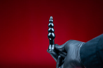 hands in black gloves holding a black silicone anal plug with sections
