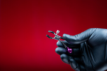 hands in black gloves holding nipple clamps for a woman for sexual bdsm games
