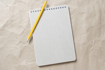 Gray notepad with white coiled spring and pencil on a background of beige crumpled craft paper. With empty space for text and design