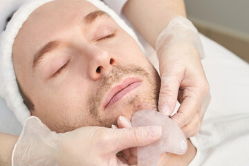 Obraz na płótnie Canvas Doctor doing skin routine. Salon maternity treatment. Health care concept. Male person. Pandemic guasha acupunture face massage. Anti age procedure