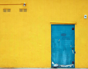 Bright blue, urban,  industrial metal door is on a bright , yellow stucco building