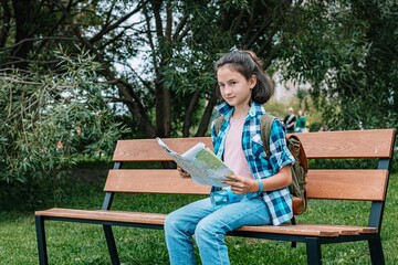 A young girl travels around the city. Cute brunette teen girl with a map is resting on a park bench. Traveling in summer vacation.