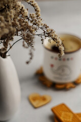 A morning, white cup of coffee with a bouquet of flowers on the table is light gray in bright light. A romantic breakfast for your beloved.