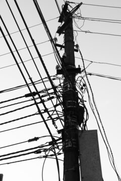 Pillar with electric wires against the sky. Urban scene with technical communications. Internet connection line. Black and white image.