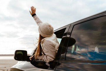 White woman wearing hat waving hand during car trip