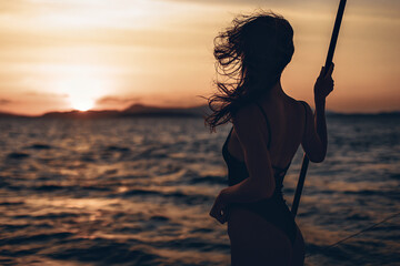 Portrait of a wonderful and interesting girl posing on her boat. Silhouette of a girl in a bikini on a sunset background. Against the backdrop of the raging sea and nature on the horizon