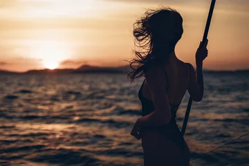 Portrait of a wonderful and interesting girl posing on her boat. Silhouette of a girl in a bikini on a sunset background. Against the backdrop of the raging sea and nature on the horizon © Semachkovsky 