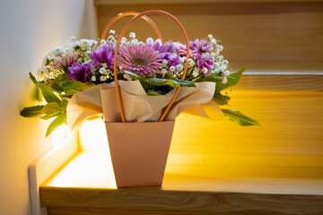 A composition of flowers in a festive box stands on the stairs with lighting. A gift for a beloved woman