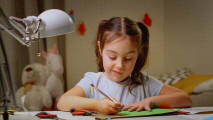 Funny cute little artist girl playing alone, drawing coloring with pencils. Smart preschooler enjoying creative art while sitting at a table in the bedroom. the concept of children's development.