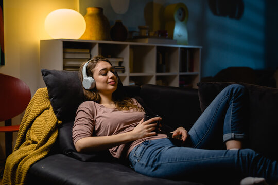 woman listening to a music on headphones at home. she is relaxing on a sofa