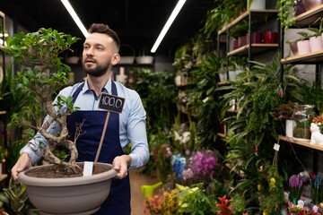 florist holding a banzai in his hands against the backdrop of a flower shop