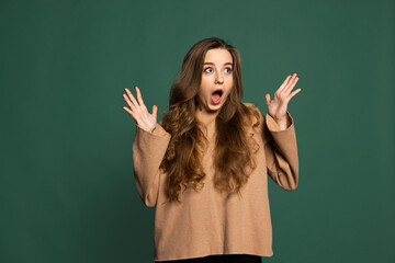 Surprised young beautiful girl wearing brown sweatshirt isolated on green background. Concept of emotions, facial expression