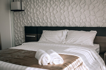 Two snow-white rolled towels are lying on the bed in the hotel bedroom