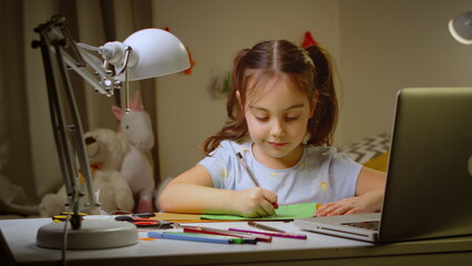 Smart cute preschool girl enjoying creativity by drawing a coloring with pencils while sitting at the table in the bedroom. the concept of children's development.