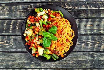 Noodles with carrots, vegetables and meat in a black plate. Food on a black Yerevan table. Basil leaves on pasta. Pasta with a mixture of vegetables. Copy space and free space for text next to food.