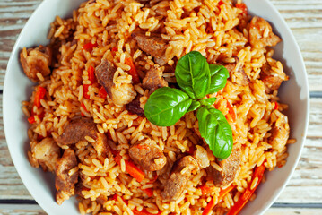 Pilaf in a white plate on a light background. Rice with basil on an old wooden board. Food on shabby wooden table. Top view.