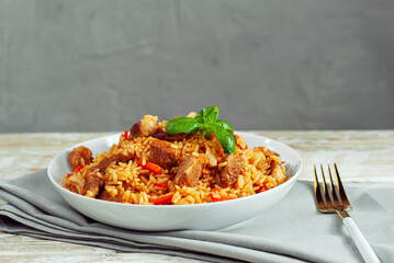 Pilaf in a white plate on a light background. Rice with basil on an old wooden board. Food on shabby wooden table.