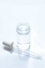 glass transparent jar and a cosmetic pipette with liquid droplets on a white background.