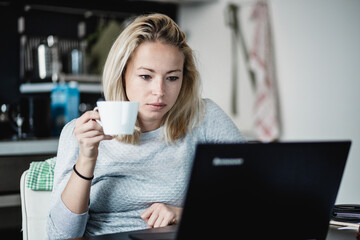 Female freelancer in her casual home clothing working remotly from her dining table in the morning. Home kitchen in the background.