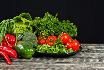 Cabbage, peppers, tomatoes, cucumbers, lettuce, cherry tomatoes, broccoli, arugula on a black background. variety of vegetables on a pile on a wooden table.