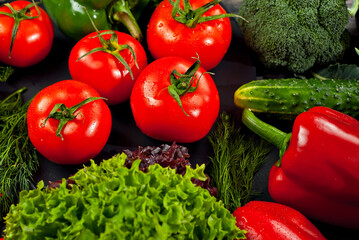 Cabbage, peppers, tomatoes, cucumbers, lettuce, cherry tomatoes, broccoli, arugula on a black background. variety of vegetables on a pile on a wooden table.