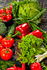 Cabbage, peppers, tomatoes, cucumbers, lettuce, cherry tomatoes, broccoli, arugula on a black background. variety of vegetables on a pile on a wooden table.