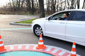 Young man in car on test track with traffic cones. Driving school