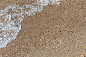 Close-up of sea foam on the sand beach with summer sunlight
