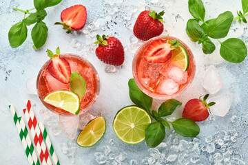 Punch cocktail. Two glasses of punch and fresh ingredients for making lemonade, infused detox water or cocktail. Strawberries, lime, mint, basil, ice cubes and shaker on grey background. Top view.