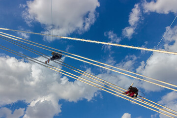 industrial mountaineers repair lighting equipment on a suspension bridge. Construction climbers hang on ropes against blue sky background with clouds