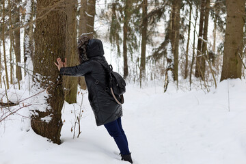Fototapeta na wymiar Woman touches the trunk of a pine tree in winter forest. Concept of unity with nature, healing properties of trees