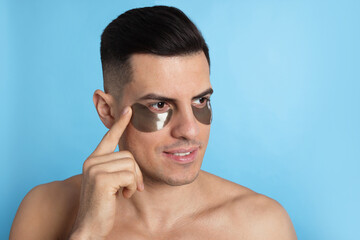 Man applying dark under eye patch on light blue background. Space for text