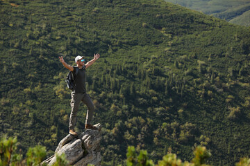 Tourist with backpack standing on rocky peak in mountains