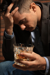 Addicted man with glass of alcoholic drink near red brick wall, closeup