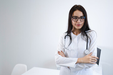 Confident female doctor standing arms crossed in office