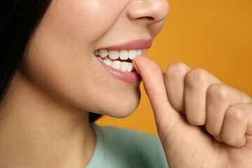 Obraz premium Young woman biting her nails on yellow background, closeup